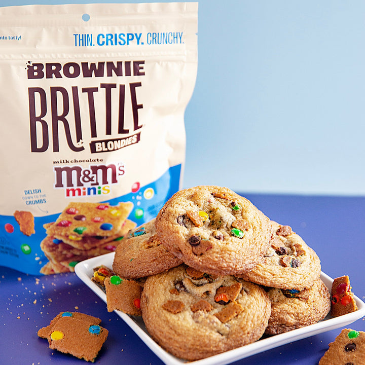 M&M'S® Minis Blondie Brownie Brittle Lifestyle image showing chocolate chip cookies made with brownie brittle on a plate on a purple surface