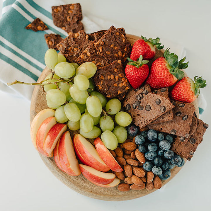 Assorted snacks including crackers, fruits, and nuts on a wooden board.