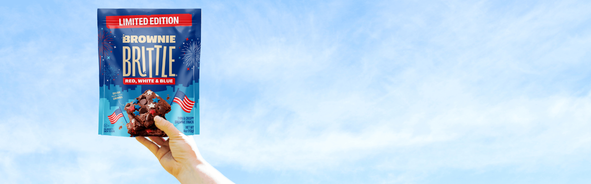 Hand holding a bag of Brownie Brittle with a blue sky background