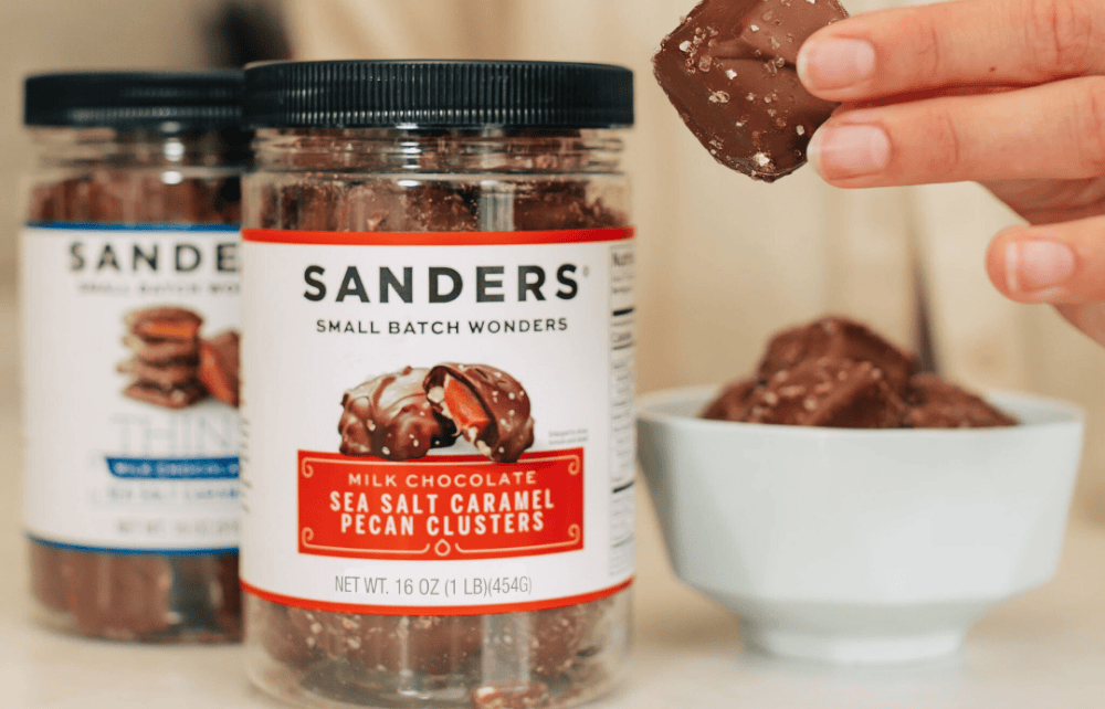 Two jars of Sanders chocolate treats with a hand holding a piece of chocolate.