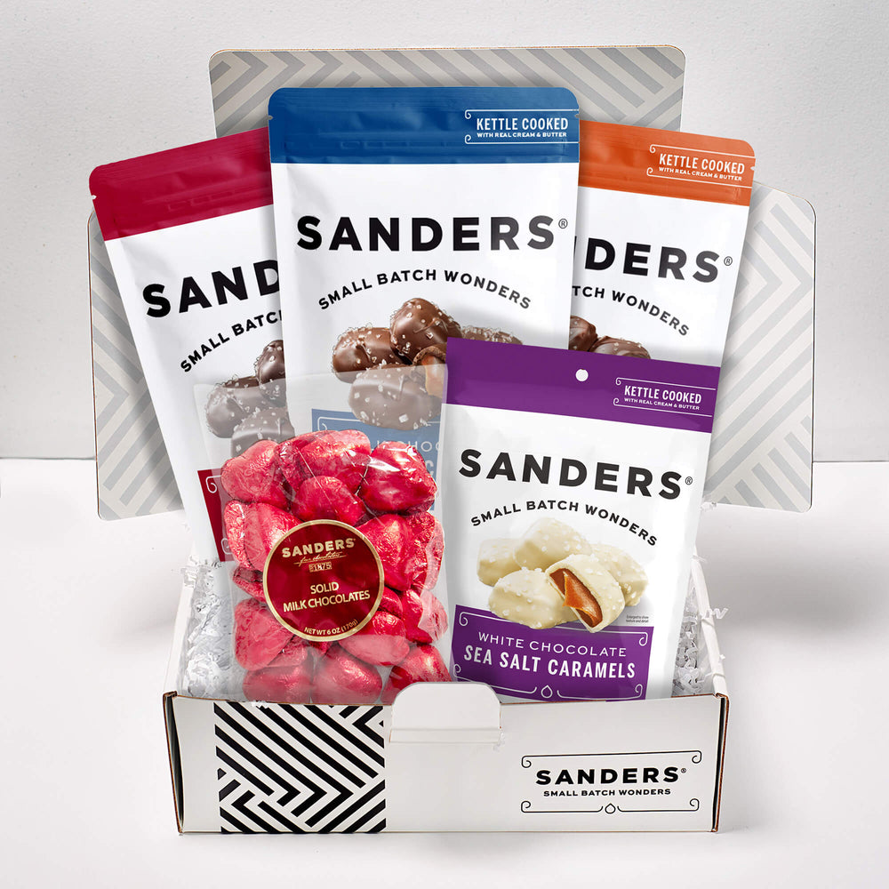 Gift box displaying assorted Sanders chocolates with colorful packaging. Includes milk chocolates and white chocolate sea salt caramels, evoking indulgence.