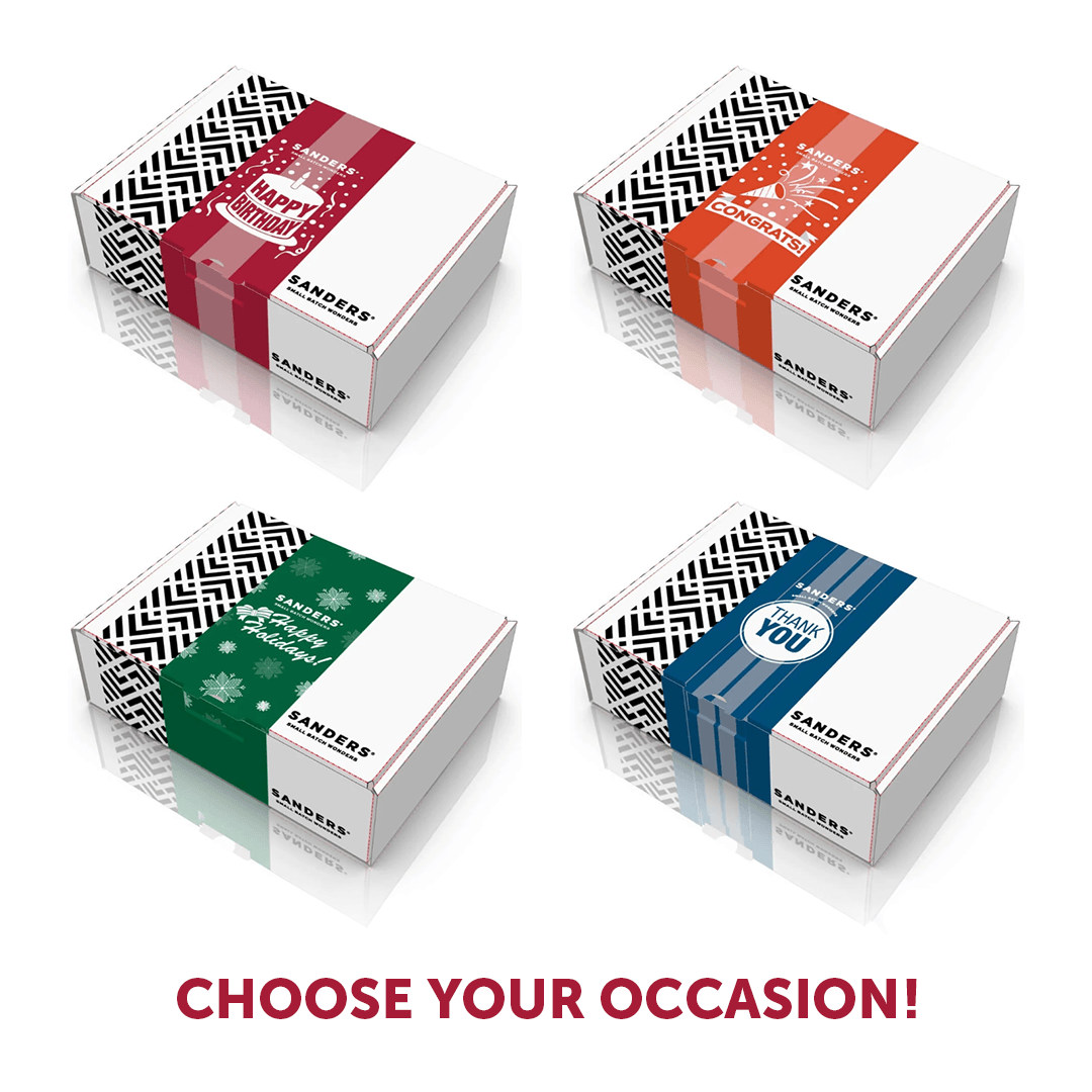 Four Sanders gift boxes arranged in a 2x2 grid on a white background with reflections, labeled for occasions: Happy Birthday, Chocolate, Christmas, and Christmas with You. The boxes are white with black chevron patterns and colored bands in red, orange, green, and blue.