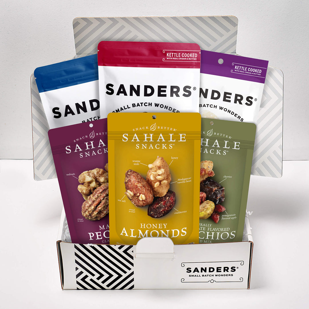 Five colorful snack bags are arranged in a box with a striped pattern. The labels read "Sanders" and "Sahale Snacks," featuring various nuts.
