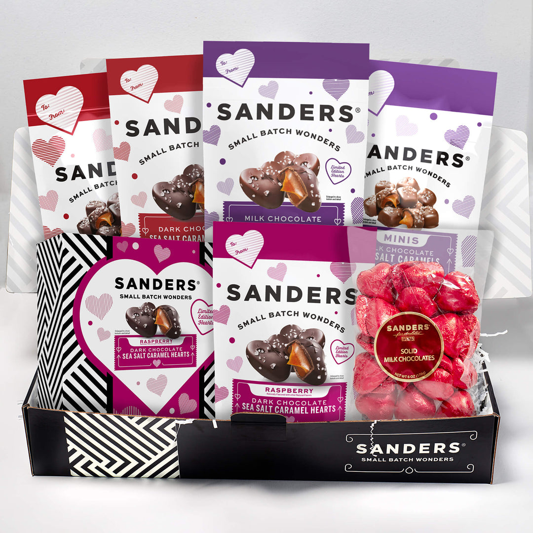 A gift box contains assorted Sanders chocolates in colorful packaging with heart designs. Visible labels include dark and milk chocolates, adding a sweet and festive feel.