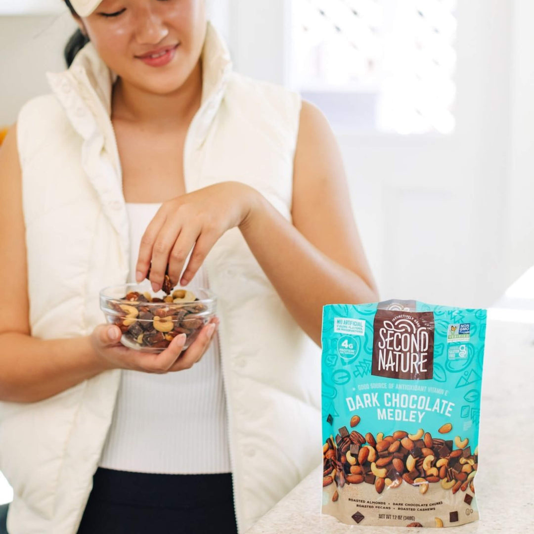 Lady grabbing Dark Chocolate Medley Trail Mix - 12 oz. in a bowl.